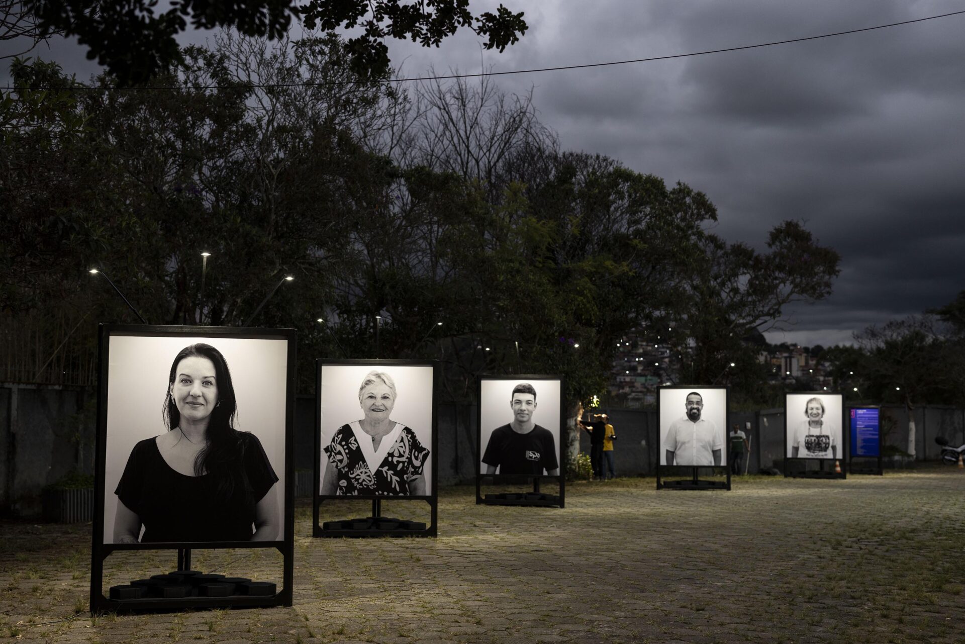 Moradores Educação: retratos em preto e branco expostos no pátio ao anoitecer