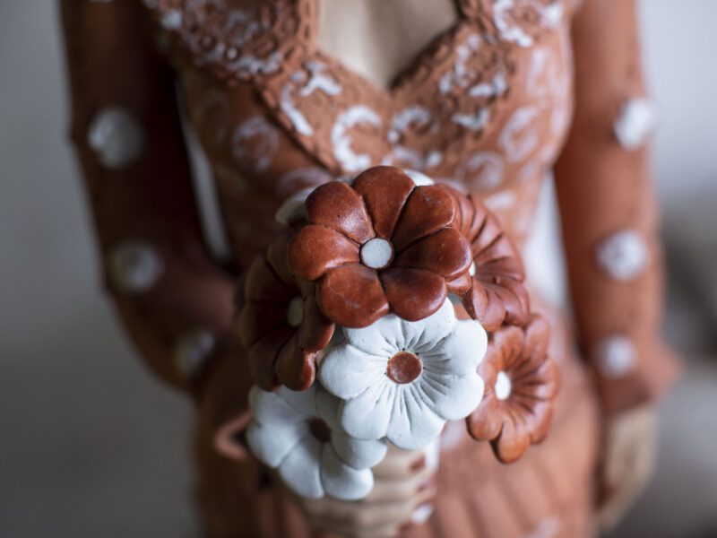 Detalhe de boneca de cerâmica do Vale do Jequitinhonha segurando buquê de flores