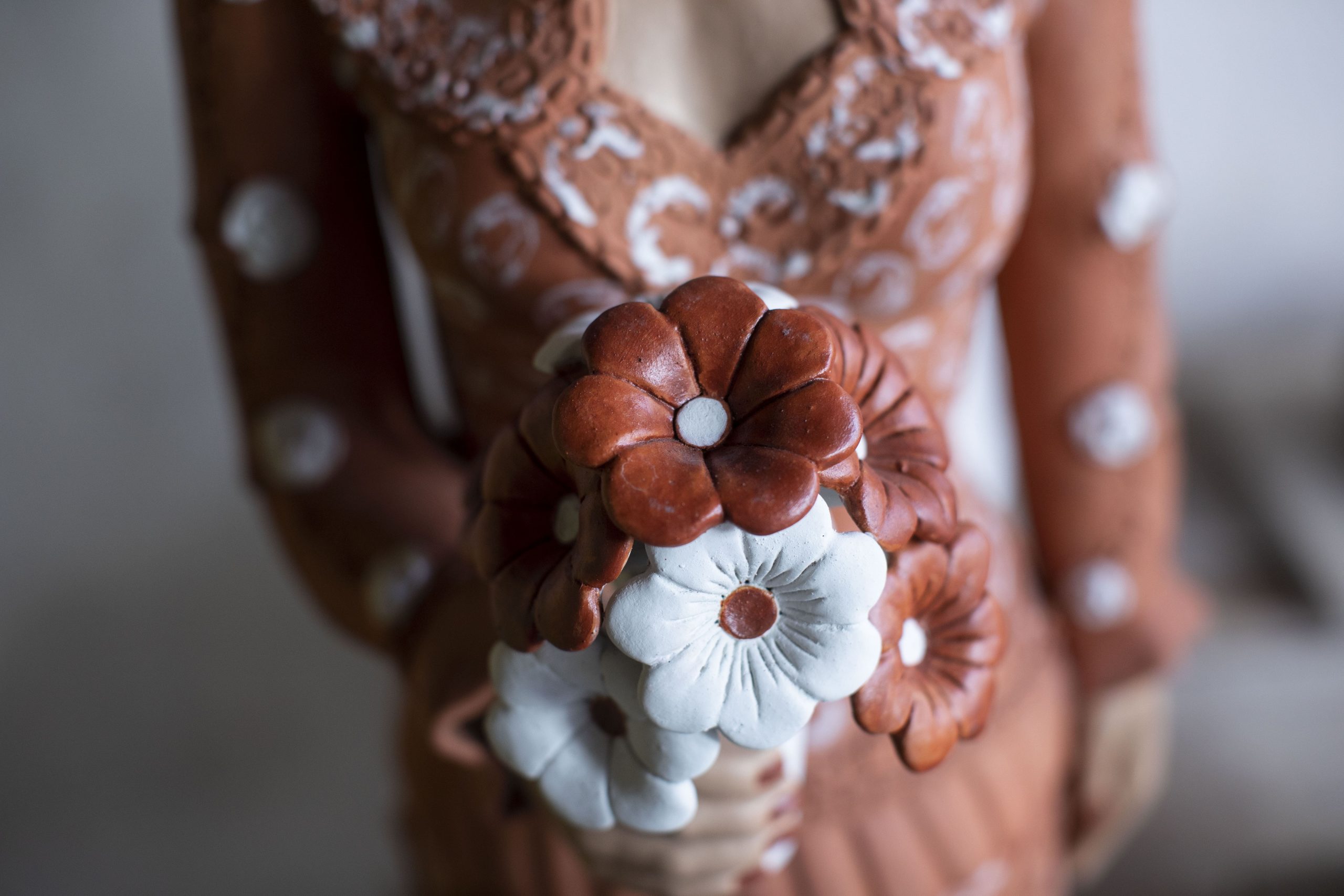 Detalhe de boneca de cerâmica do Vale do Jequitinhonha segurando buquê de flores