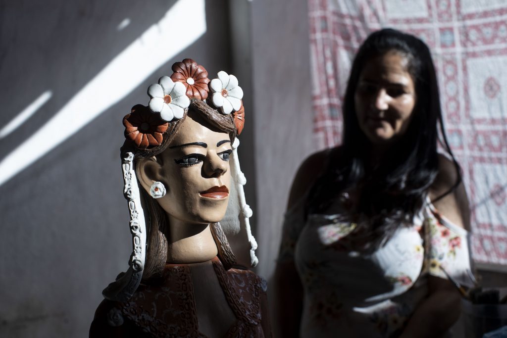 Artesã ao lado de boneca de cerâmica com coroa de flores, no Vale do Jequitinhonha