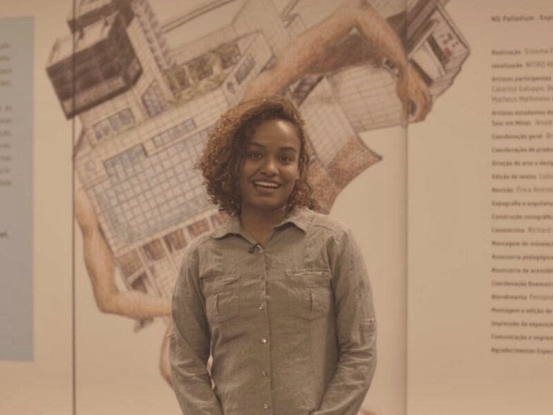 Ariene Reis sorri diante de painel da exposição ENTRE