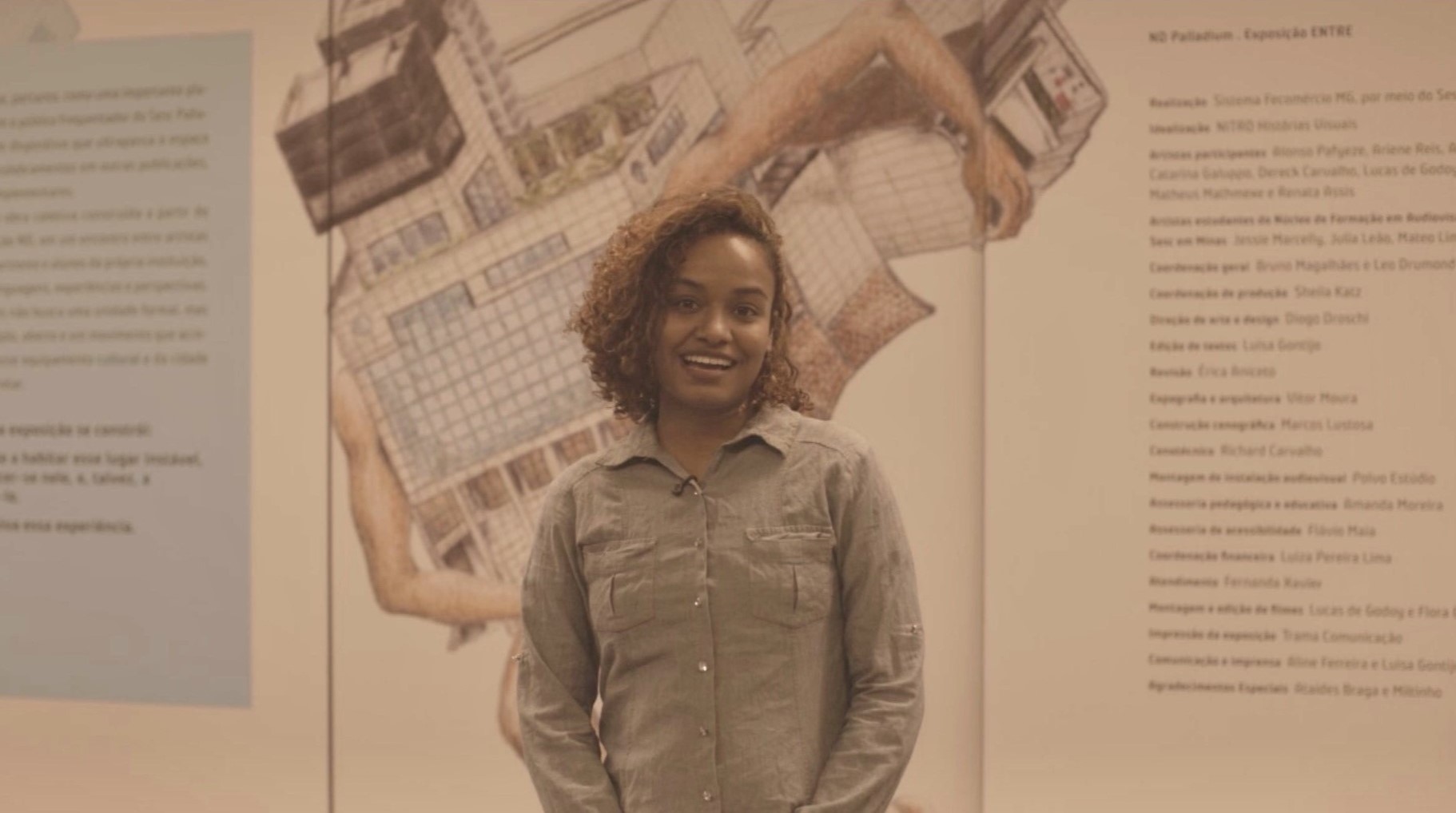 Ariene Reis sorri diante de painel da exposição ENTRE