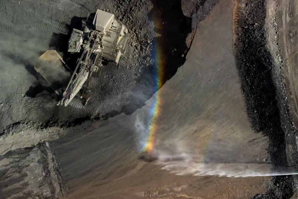 Lundin Mining: escavadeira em mina a céu aberto com arco-íris formado pela água