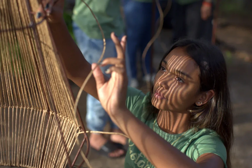 Retratos do Cooperativismo: artesã trança fibra natural com a luz desenhando sombras no rosto