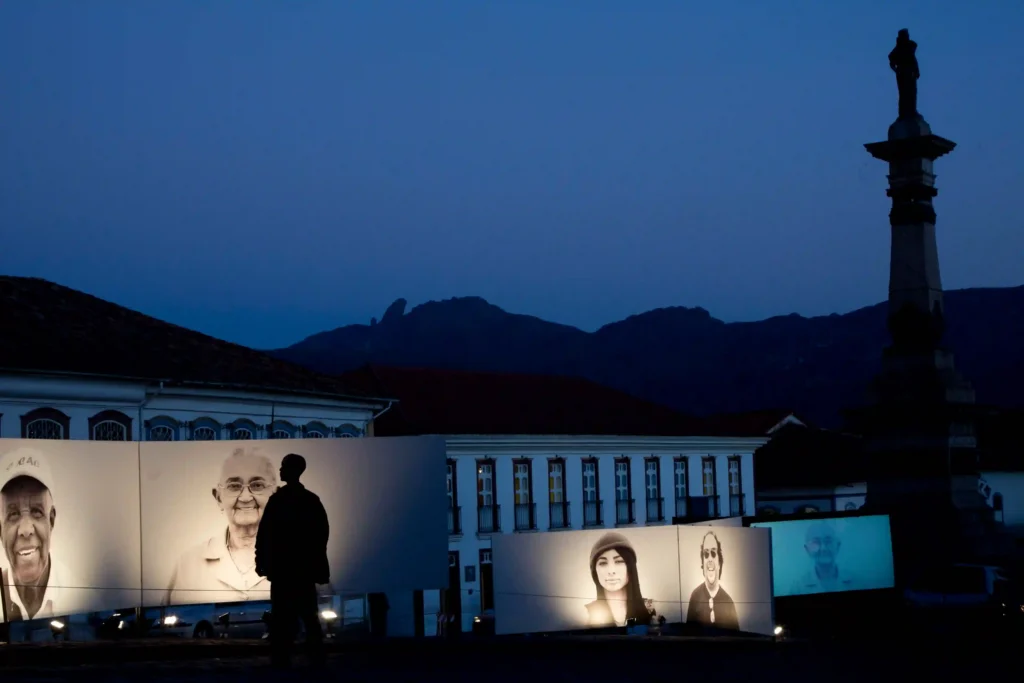 Projeto Moradores: retratos projetados em casarões coloniais ao anoitecer, com silhueta de visitante