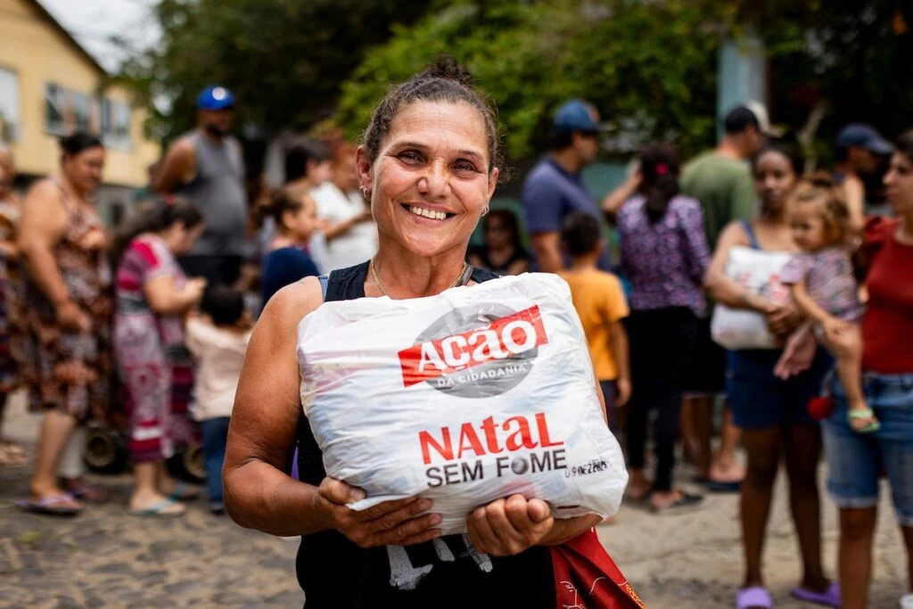 Ação da Cidadania, Natal Sem Fome: mulher sorridente segura sacola de doação na rua