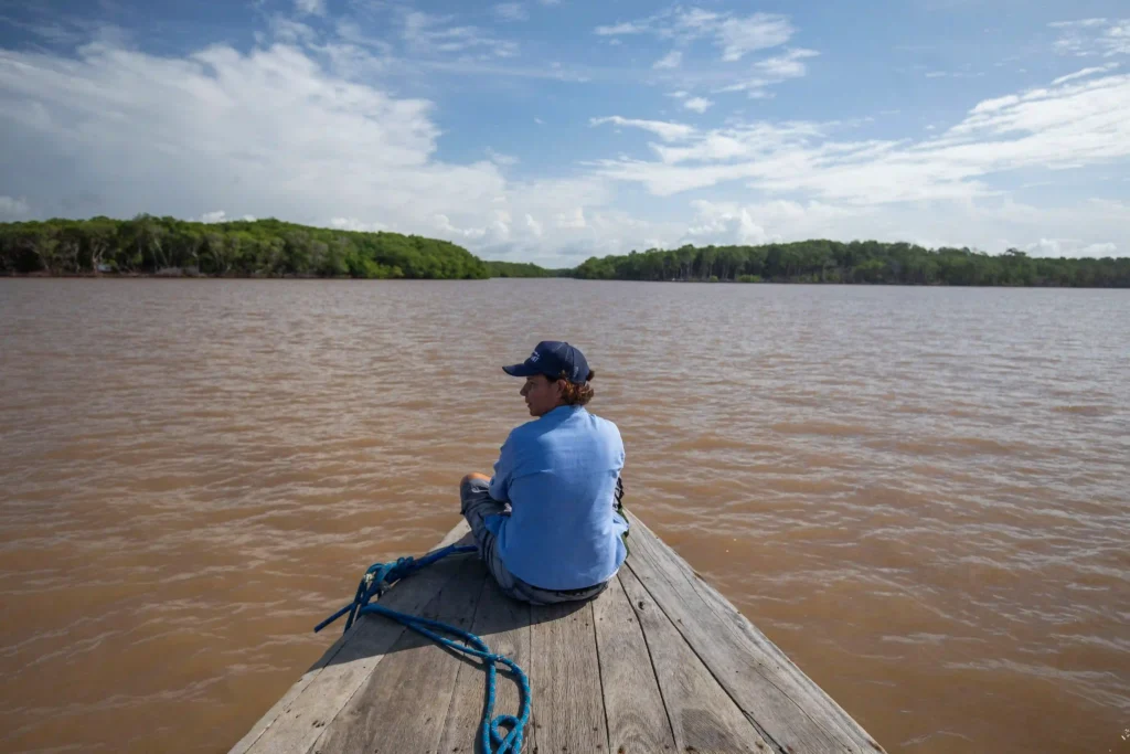Mulheres na Conservação: pesquisadora sentada na proa de um barco em rio de águas barrentas