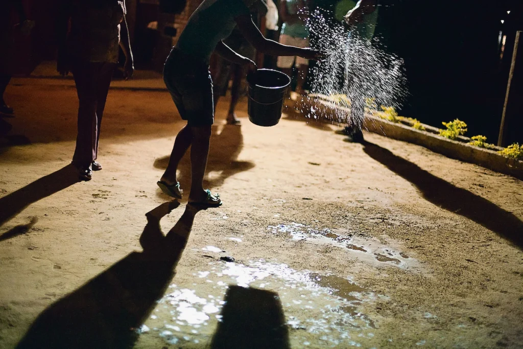Os Chicos: pessoas jogam água em terreiro iluminado à noite