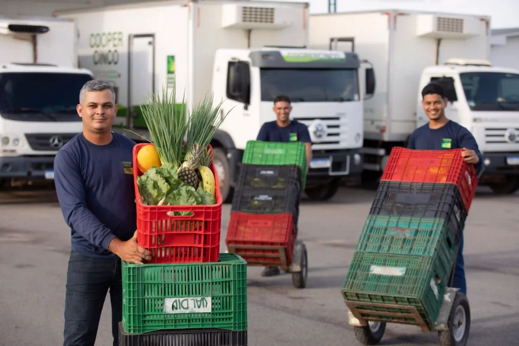 Retratos do Cooperativismo: cooperados com caixas de frutas e verduras diante de caminhões