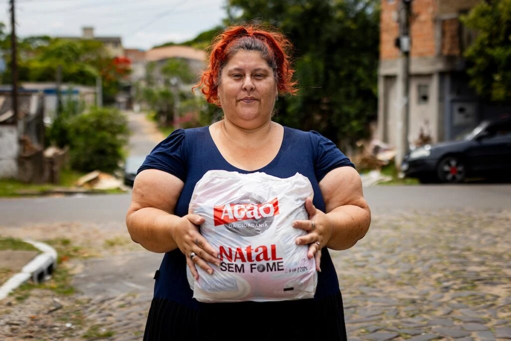 Ação da Cidadania, Natal Sem Fome: mulher segura sacola de doação em rua de paralelepípedos
