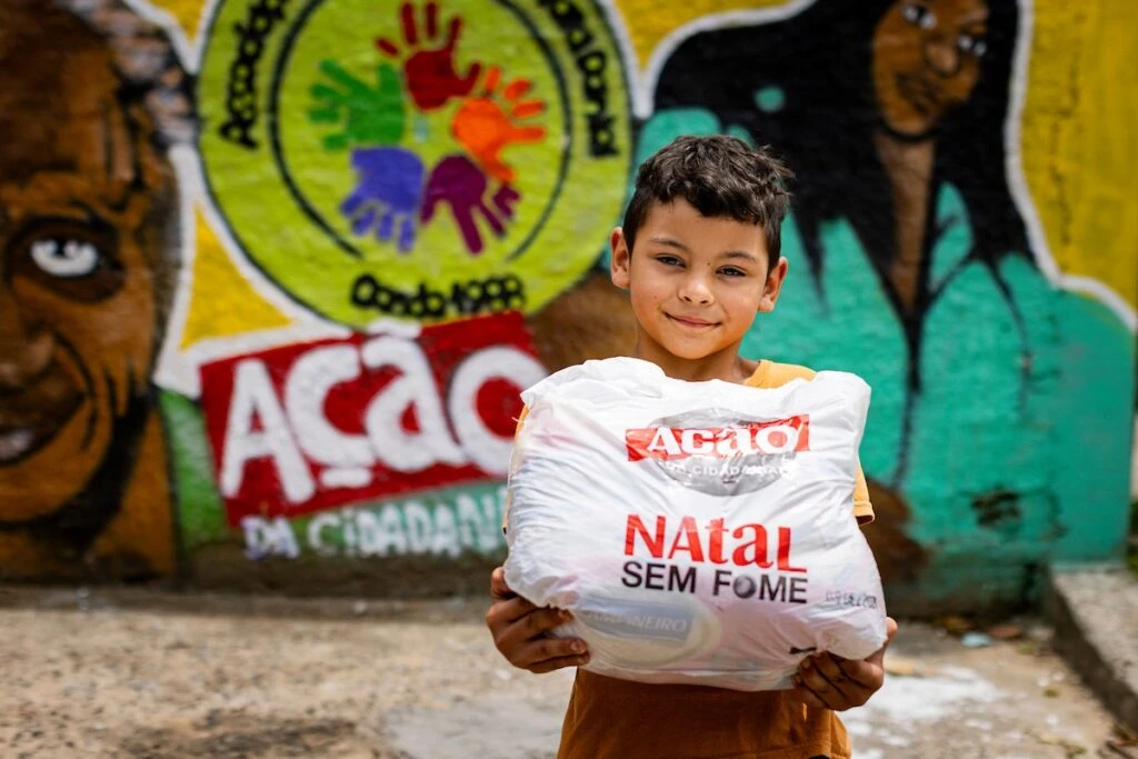 Ação da Cidadania, Natal Sem Fome: menino segura sacola de doação diante de mural grafitado