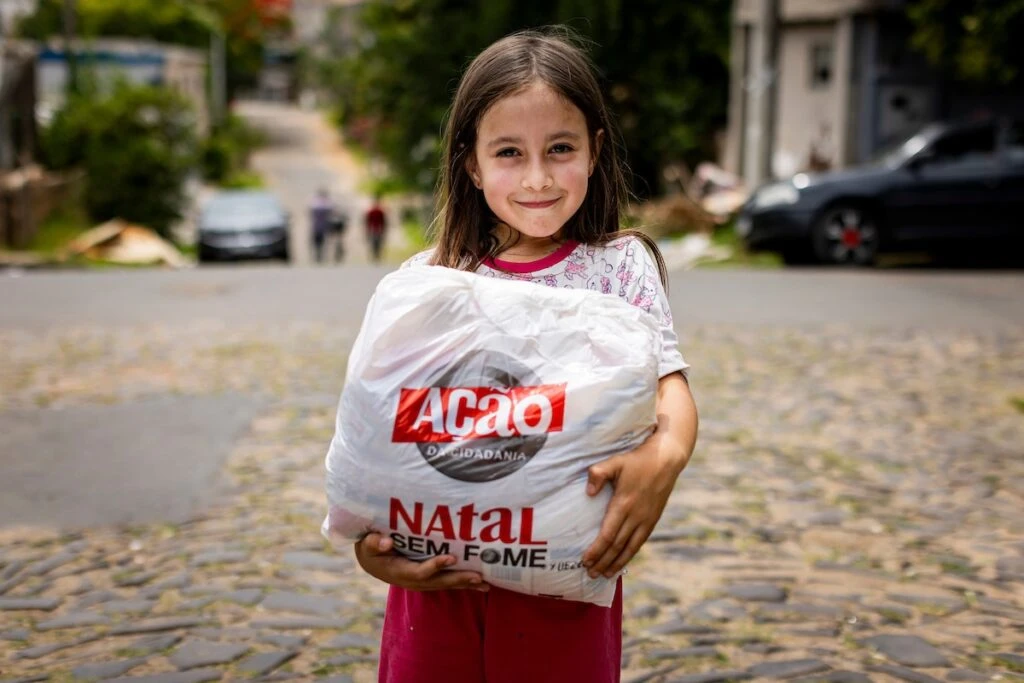 Ação da Cidadania, Natal Sem Fome: menina segura sacola de doação em rua de paralelepípedos