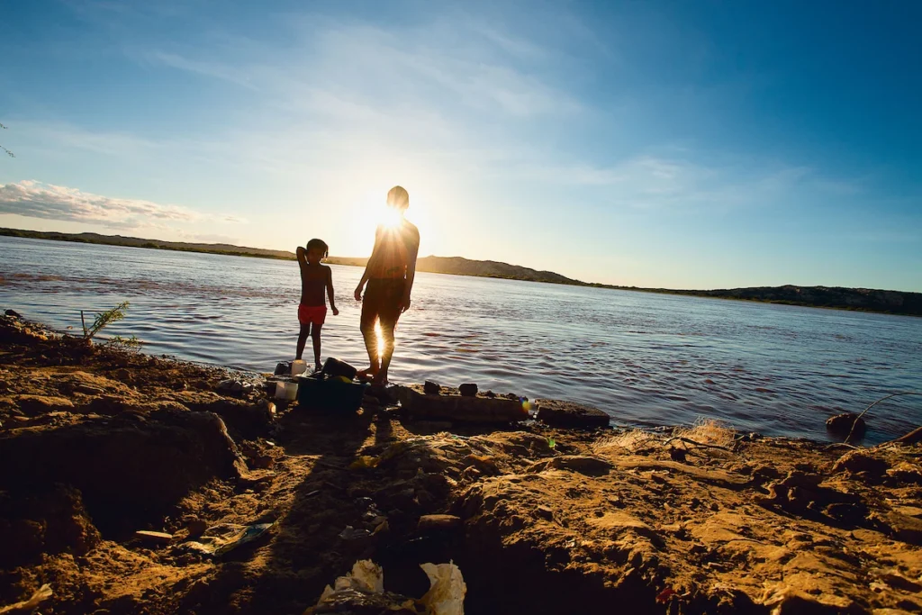 Os Chicos: mãe e filha em silhueta na margem do rio São Francisco ao entardecer