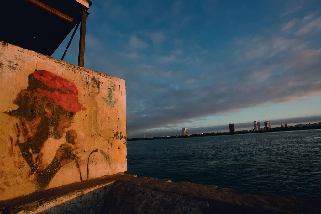 Os Chicos: pintura de rosto em muro à beira do rio, com a cidade ao fundo