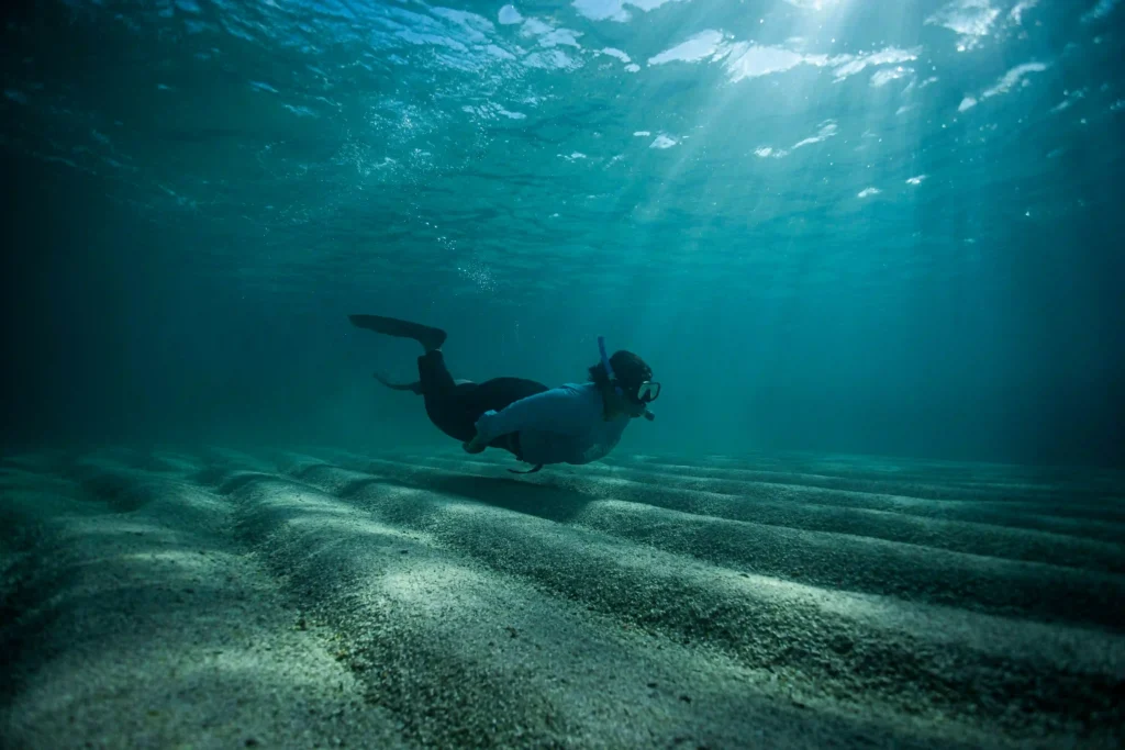 Mulheres na Conservação: pesquisadora mergulha sobre fundo de areia em águas cristalinas