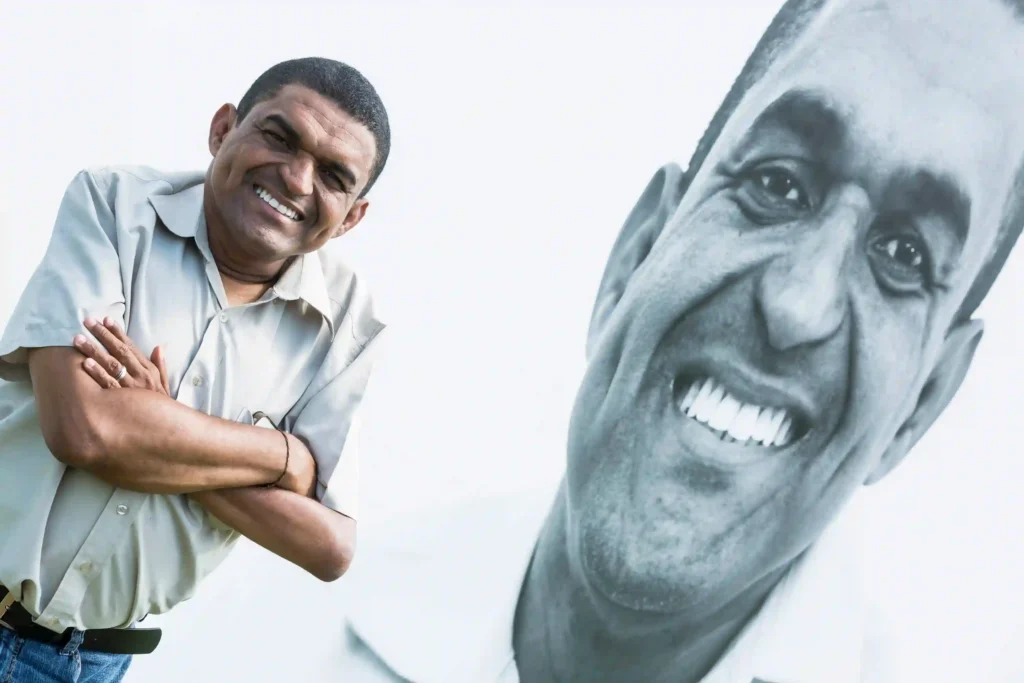 Projeto Moradores: morador sorridente ao lado do seu próprio retrato em grande formato