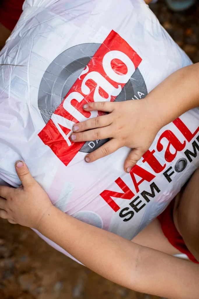 Ação da Cidadania, Natal Sem Fome: mãos de criança abraçando sacola de doação, vista de cima