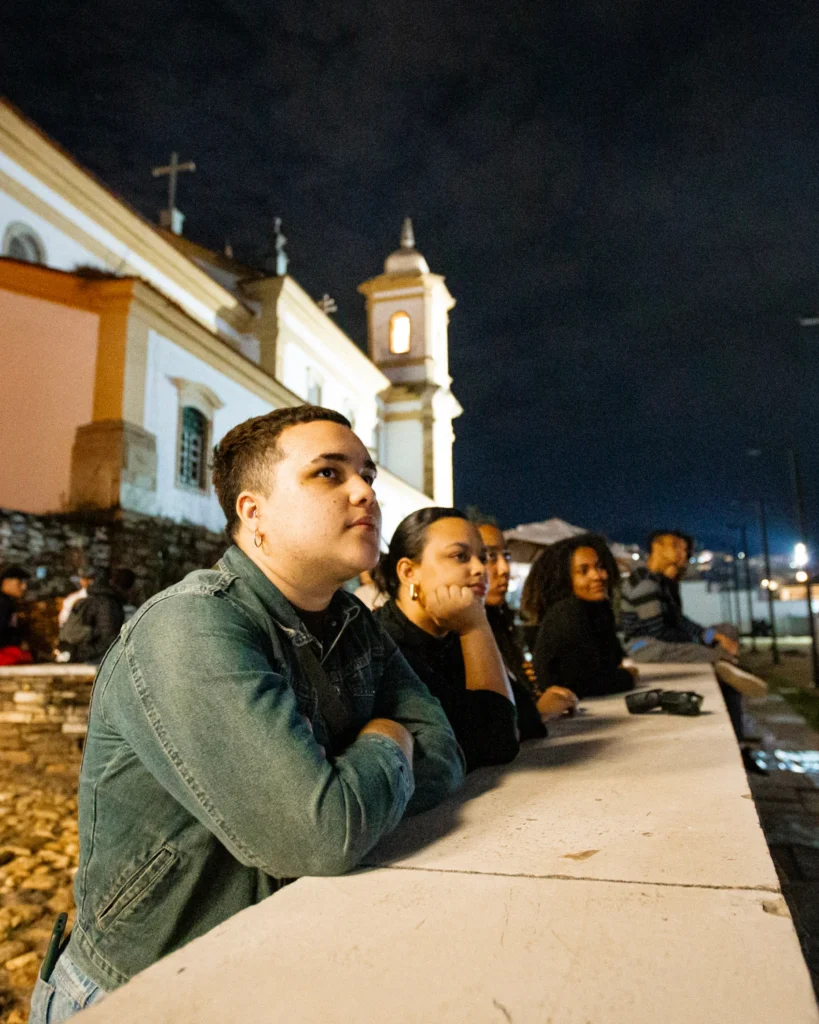 Exibição de Tempo Vário em Mariana: jovens apoiados em mureta assistem ao filme