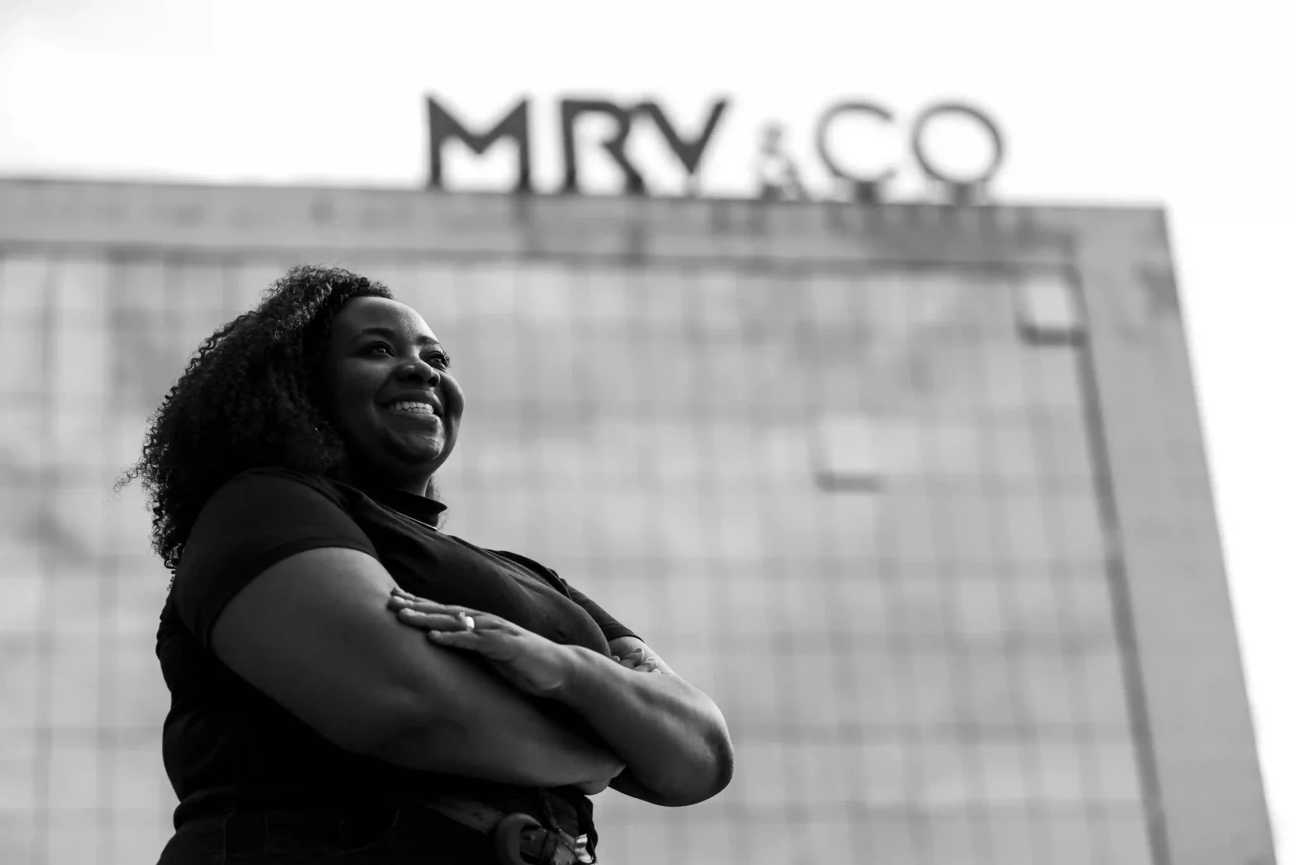 Relatório MRV&CO: colaboradora sorridente de braços cruzados diante da sede