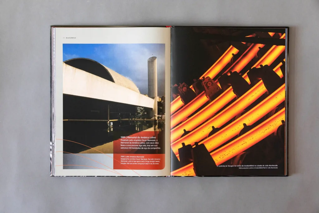 Livro ArcelorMittal 100 anos aberto com fotos de arquitetura e de aço incandescente