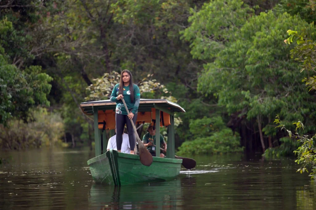 Retratos do Cooperativismo: mulher conduz barco a remo em rio cercado de mata