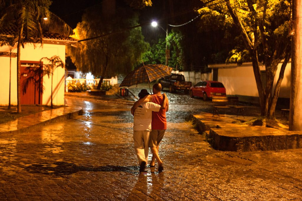 Tramas: casal caminha sob guarda-chuva em rua molhada à noite