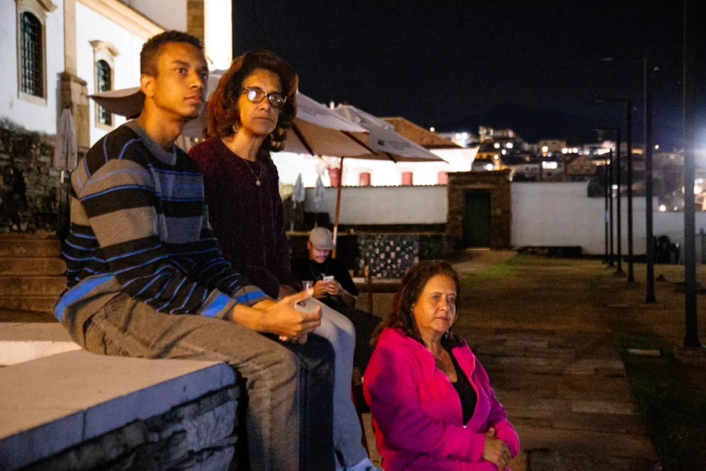 Exibição de Tempo Vário em Mariana: família sentada em mureta assiste ao filme