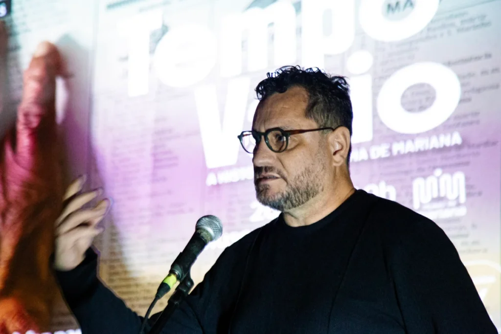 Exibição de Tempo Vário em Mariana: diretor fala ao microfone diante do cartaz do filme
