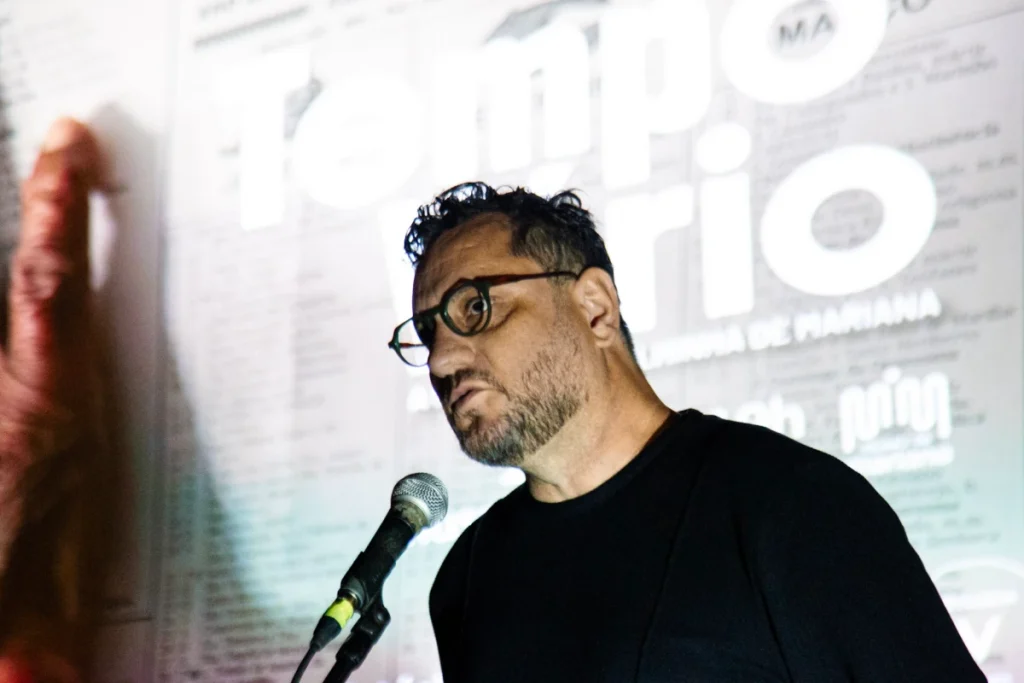 Exibição de Tempo Vário em Mariana: diretor fala ao microfone diante do cartaz do filme