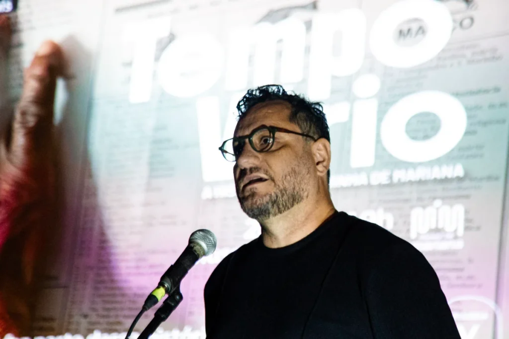 Exibição de Tempo Vário em Mariana: diretor fala ao microfone diante do cartaz do filme