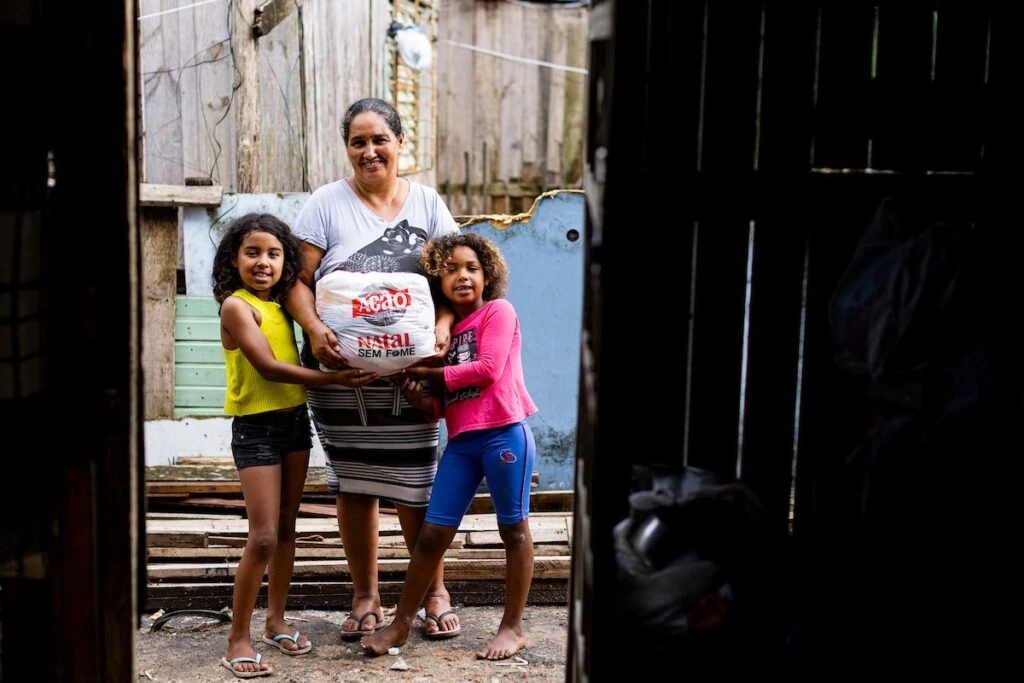 Ação da Cidadania, Natal Sem Fome: mãe e filhas com sacola de doação diante de casa