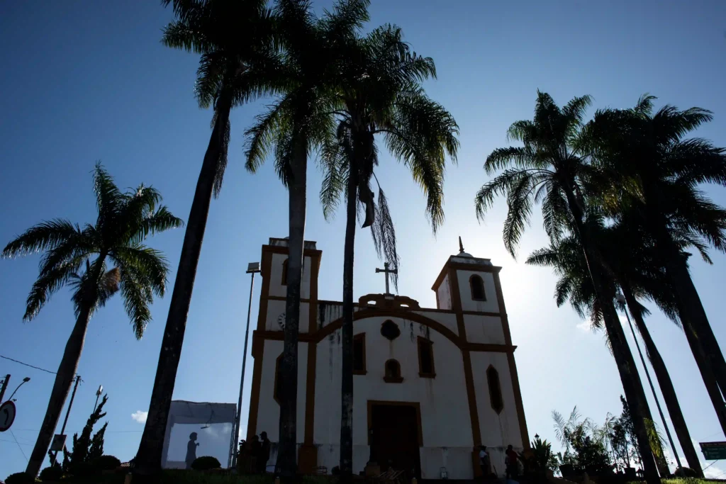 Projeto Moradores: igreja colonial entre palmeiras com cubo de exposição ao lado