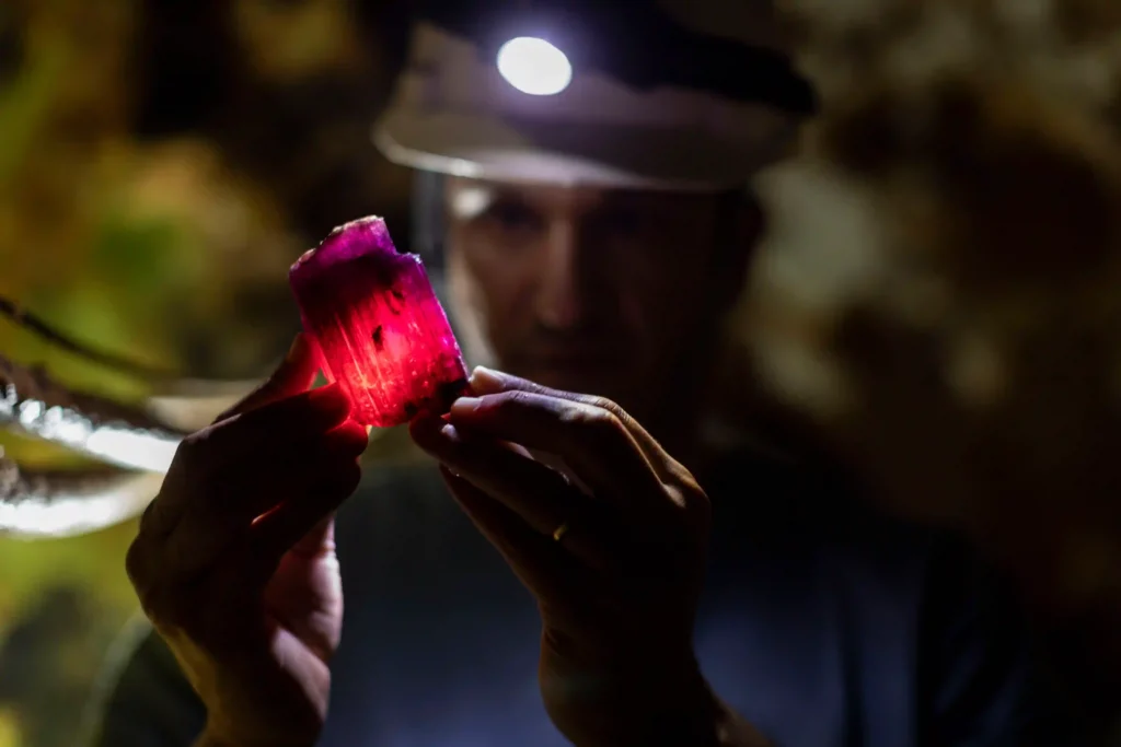 Mina do Cruzeiro: minerador com lanterna de cabeça examina turmalina rosa contra a luz