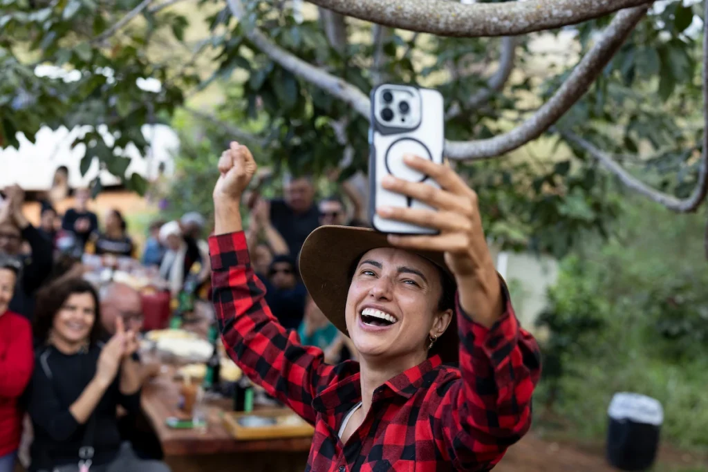 Sebrae Origem e Experiências Turísticas: mulher de chapéu faz selfie em almoço festivo ao ar livre
