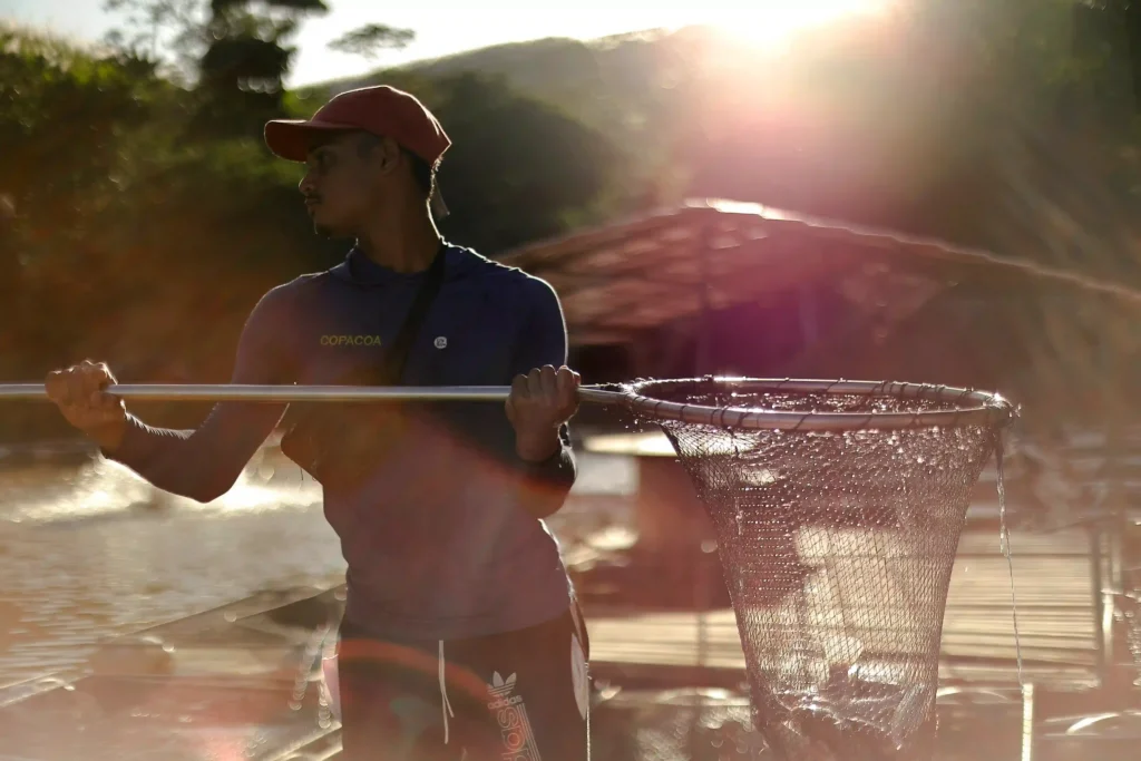 Retratos do Cooperativismo: pescador com puçá na beira do rio contra o sol