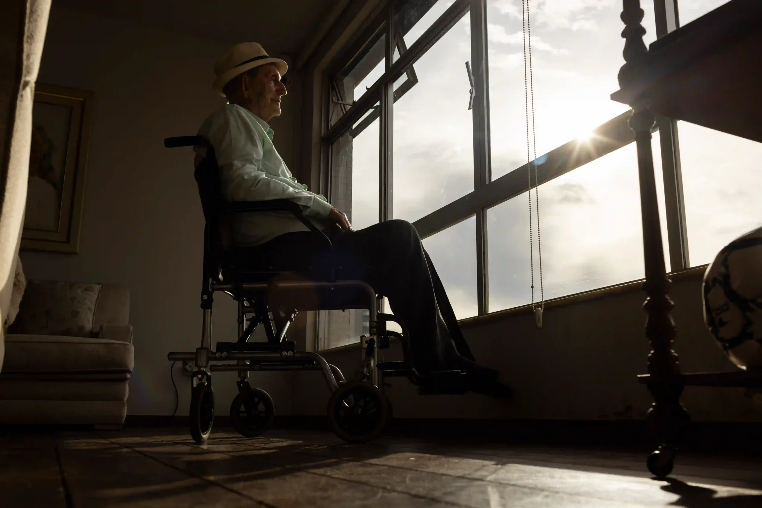 Centenários: senhor em cadeira de rodas junto à janela iluminada