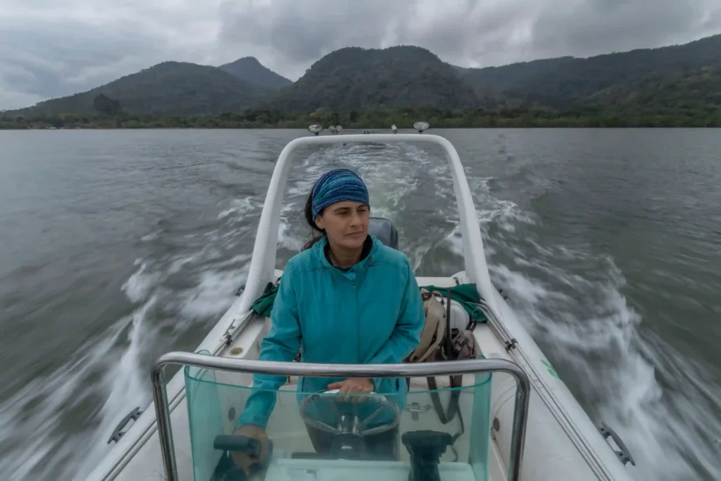 Mulheres na Conservação: pesquisadora pilota barco em baía cercada de montanhas