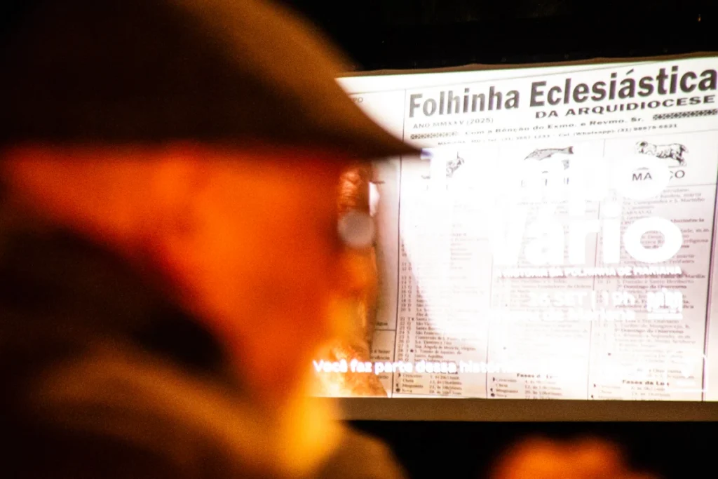 Exibição de Tempo Vário em Mariana: senhor de boina diante da tela com a Folhinha Eclesiástica