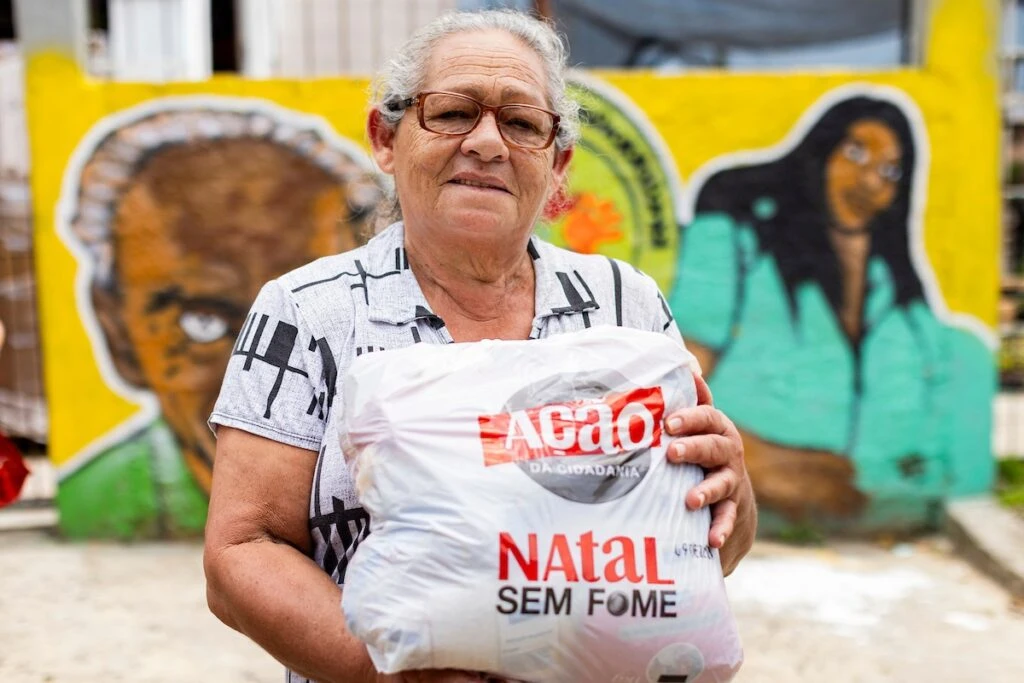 Ação da Cidadania, Natal Sem Fome: senhora segura sacola de doação diante de mural grafitado