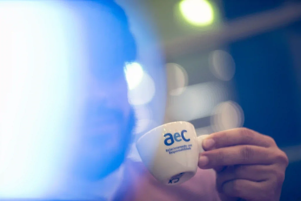 AEC: mão segura xícara de café com logotipo da AEC