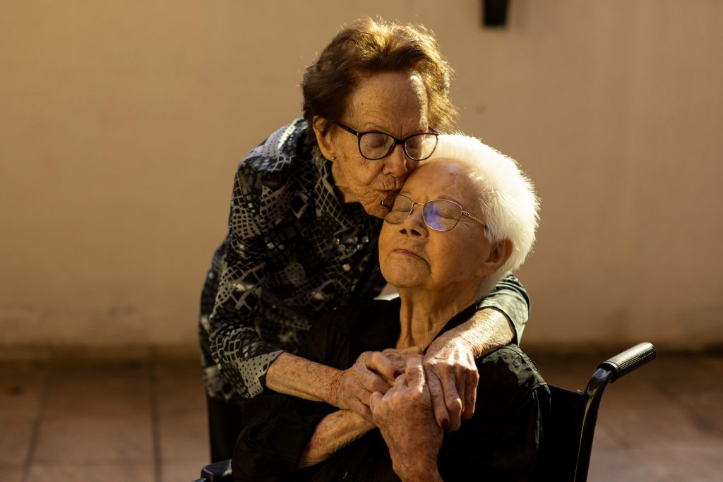 Centenários: Gercy beija a testa da irmã Lourdes, sentada em cadeira de rodas, em Belo Horizonte